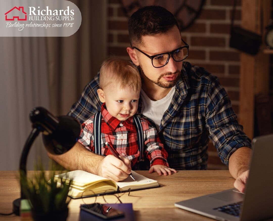A father holding his son sitting at a desk viewing a computer.